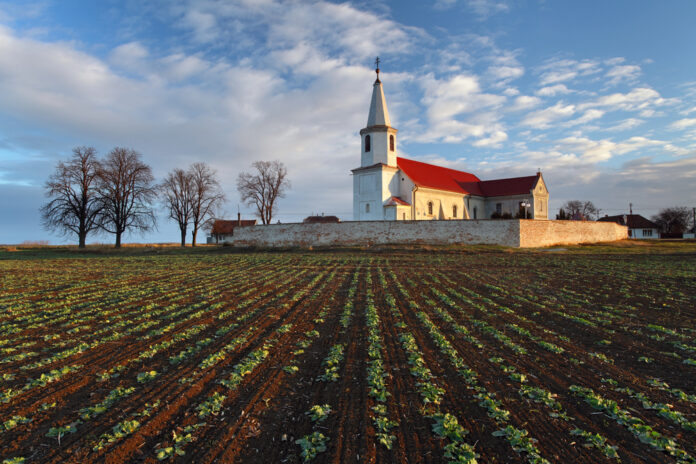 Ackerfeld und eine Kirche im Hintergrund unter blauem Himmel mit einigen Wolken.