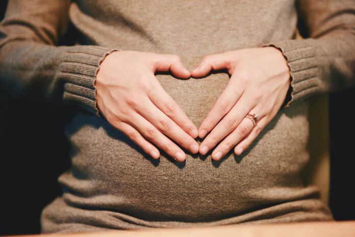 Schwangere Frau formt ein Herz mit ihren Händen auf dem Bauch.