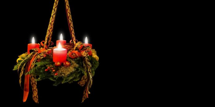 Adventskranz mit vier brennenden roten Kerzen.