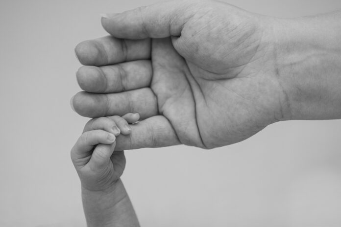 Babyhand greift nach kleinem Finger von einem Erwachsenen.