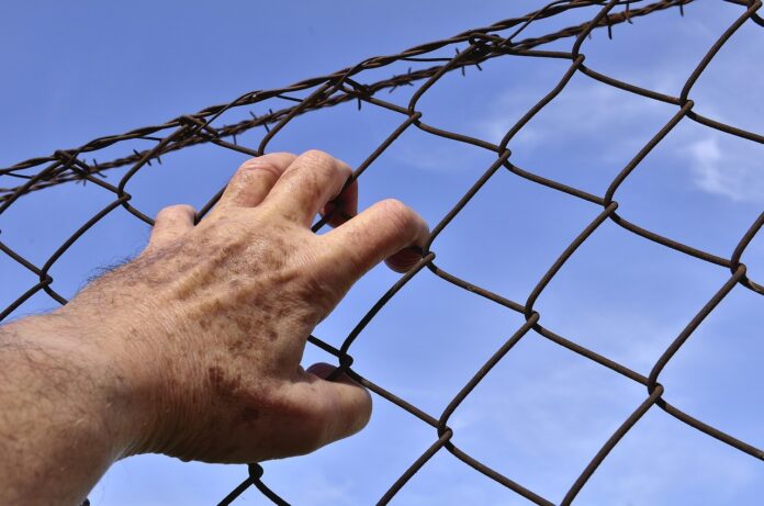 Eine Hand am Stacheldrahtzaun, als Symbol der Einschränkung.