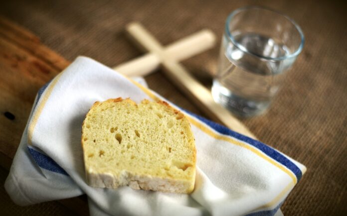 Ein Stück Brot auf einem Tuch, ein Holzkreuz und ein Glas Wasser als Symbol für die Fastenzeit.