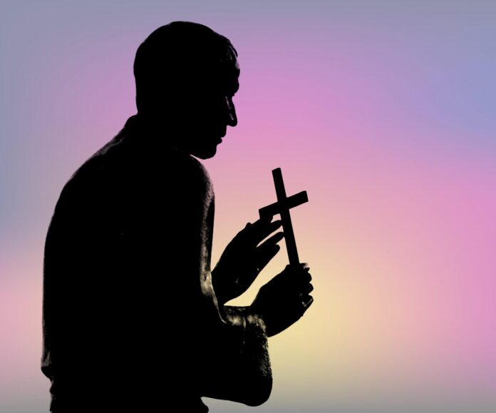 Priesterstatue hält ein Kreuz