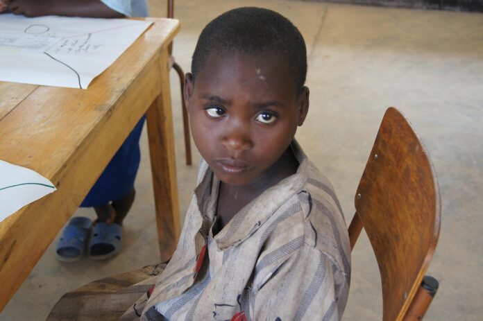 Ein Junge in Afrika sitzt an einer Schulbank und blickt traurig. Ein Symbolbild, dass Schuldenabbau in Entwicklungsländern häufig zu lasten der Bildung geht.
