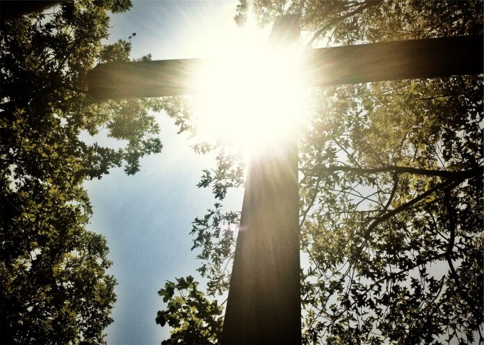 Die Sonne strahlt durch ein großes Kreuz.