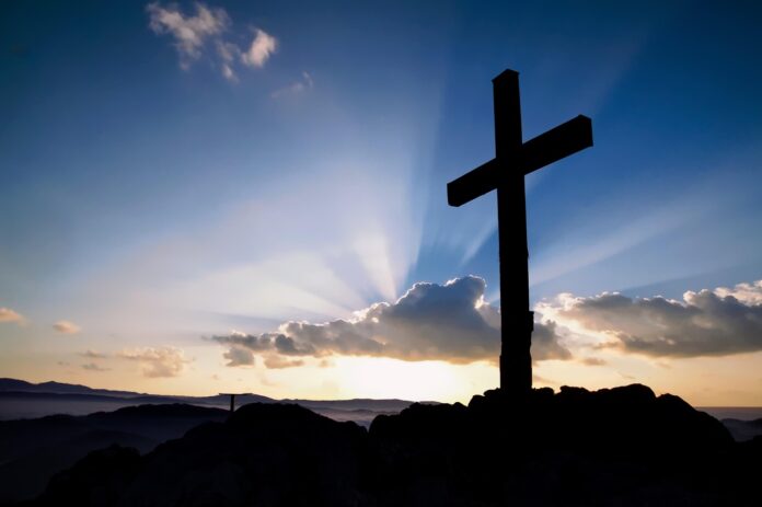 Kreuz im Vordergrund im Hintergrund Licht, das Wolken durchbricht.