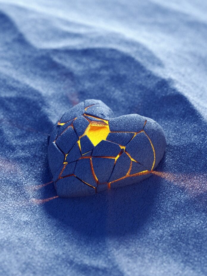 Herz im Sand, das von einem Teelicht erleuchtet wird