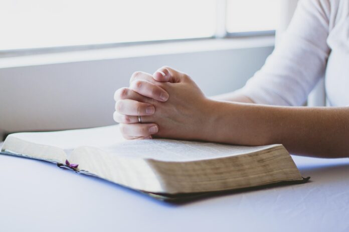 Eine Person betet mit überkreuzten Fingern über der Bibel.