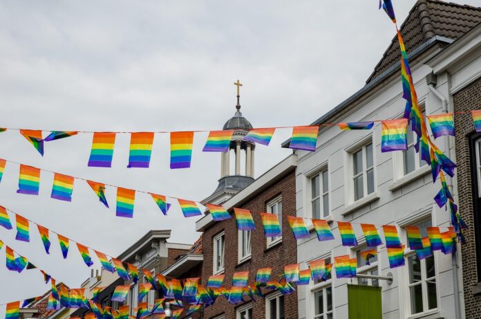 Im Vordergrund hängen Regenbogenflaggen an mehreren Leinen - im Hintergrund ist ein Kirchturm zu sehen.