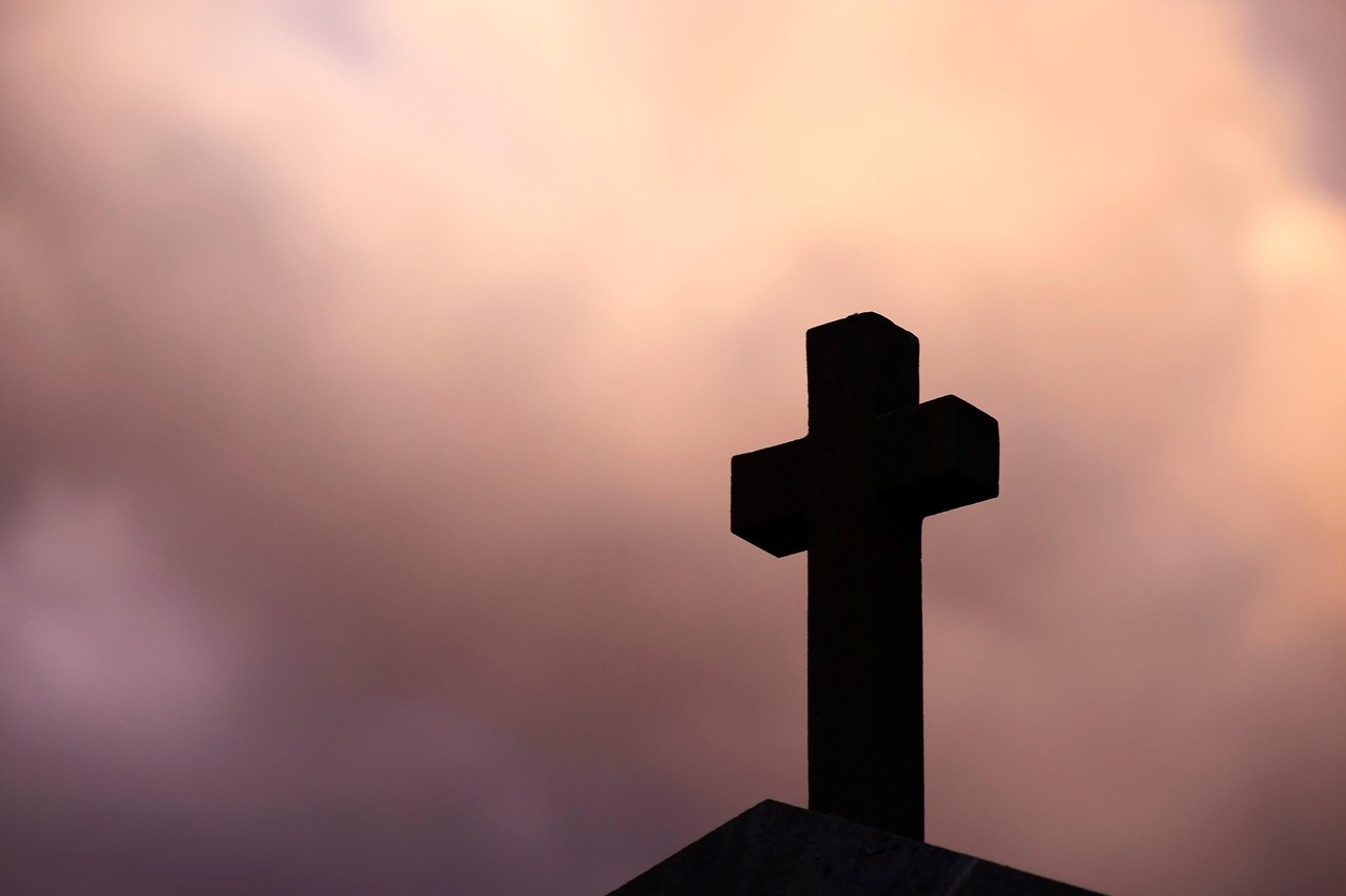 Kreuz im Vordergrund. Im Hintergrund der Abendhimmel