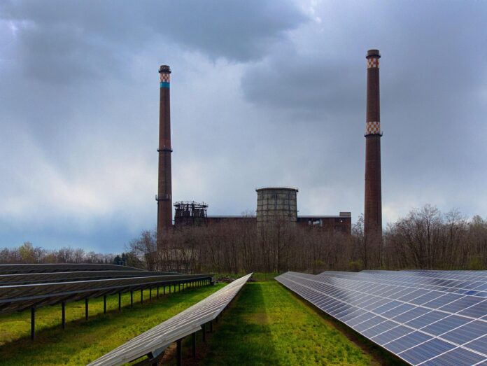 Im Vordergrund ein Solarfeld und im Hintergrund zwei große Schornsteine. Symbolbild für die UN-Nachhaltigkeitsziele