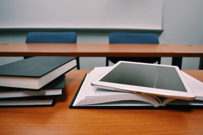 Schulbank mit mehreren Büchern und einem Tablet darauf.