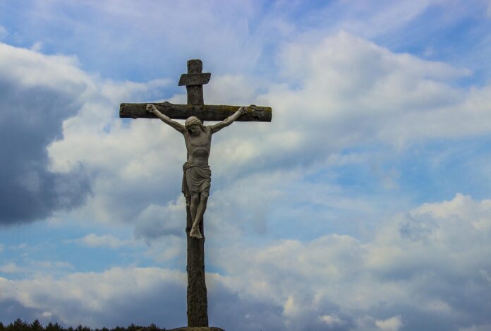 Kreuz mit Jesusfigur vor blauem Himmel.