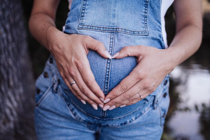 Schwangere Frau hält die in Hände in Form eines Herzens vor den Bauch