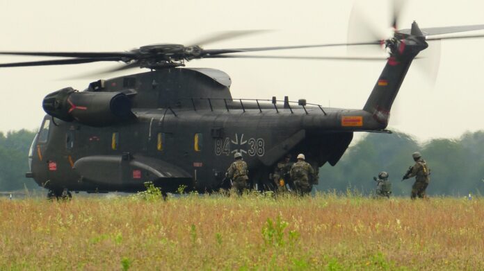 Militärhubschrauber auf dem Feld. Bewaffnete Soldaten laufen darauf zu.