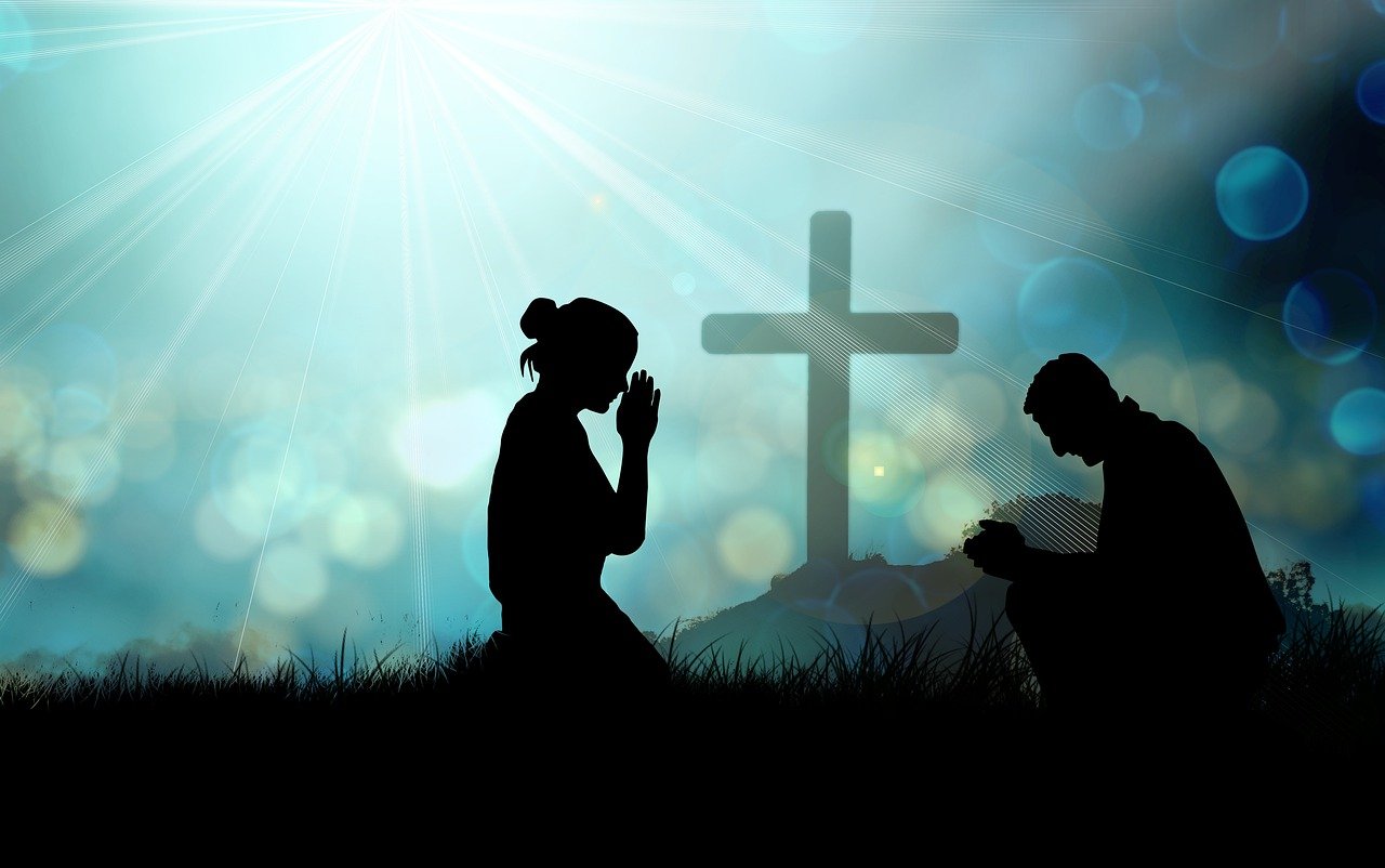 Zwei Menschen beten vor einem Kreuz